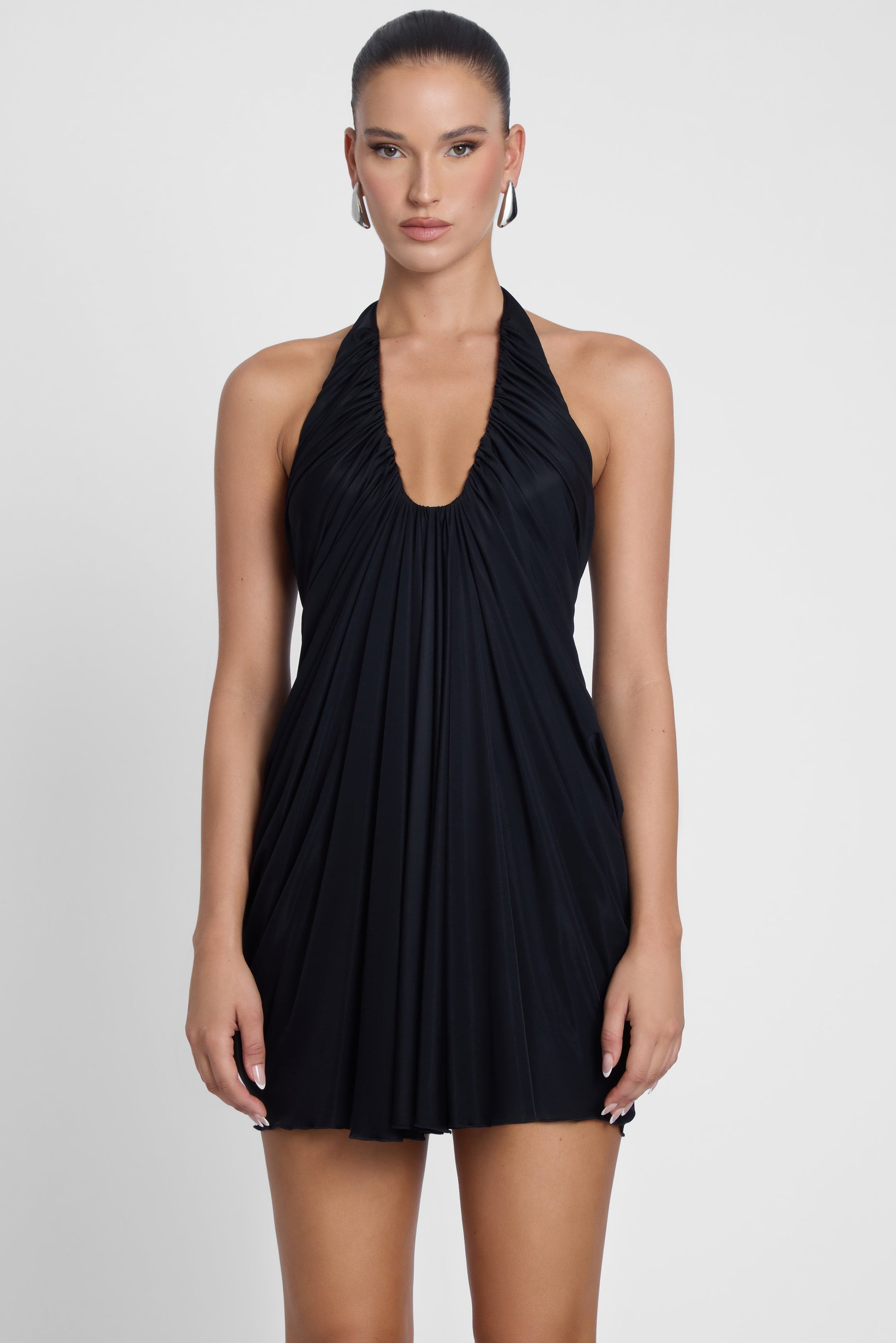 Model is wearing Odyssey Drape Mini Dress Black, front view.